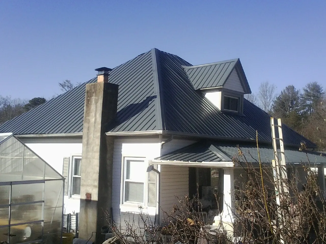Dark blue standing seam metal roof on a white farmhouse with dormer — Slate & Tile Roof Repair by Roofing Brothers in Snowmass