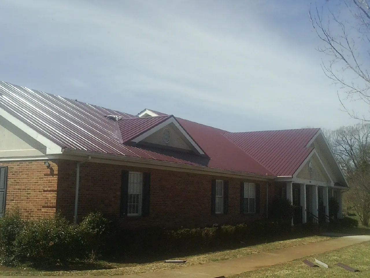Red metal roof with gabled entries on a long brick building, from a Hail Damage Roof Repair job in Snowmass