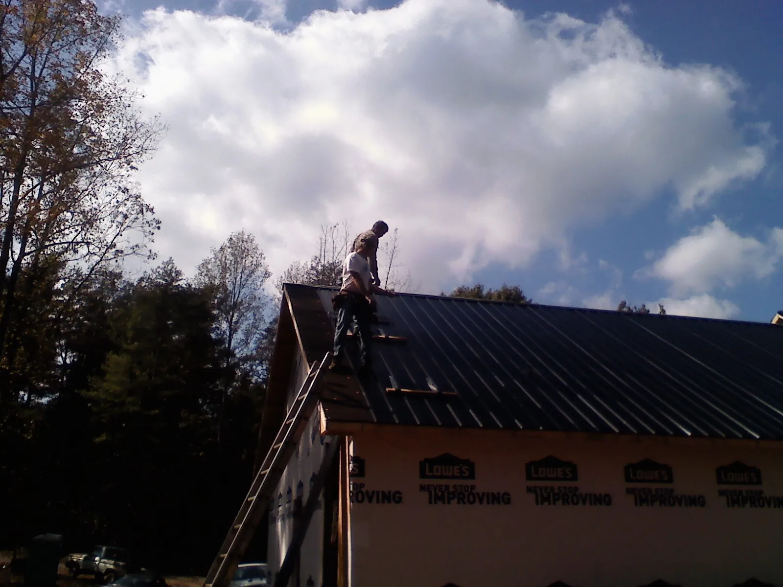 Roofer fastening dark metal panels high against a cloudy sky, from a Roof Inspection job in Snowmass